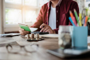 A businessman using pen, calculator recording money coins.