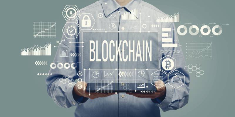 A man holding a tablet with the word blockchain in the middle and graphical representations related to block chain around it.