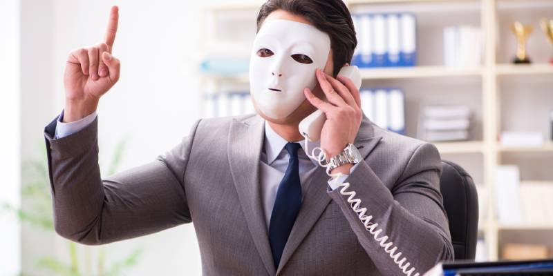 A businessman speaking on a land phone with mask on his face.