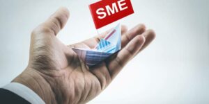 A businessman's hand holding a boat made of paper graph with the word SME written on its flag.