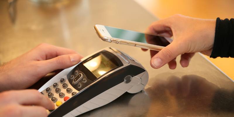 Image of a hand holding an EDC machine and another one holding a smartphone to make a payment.